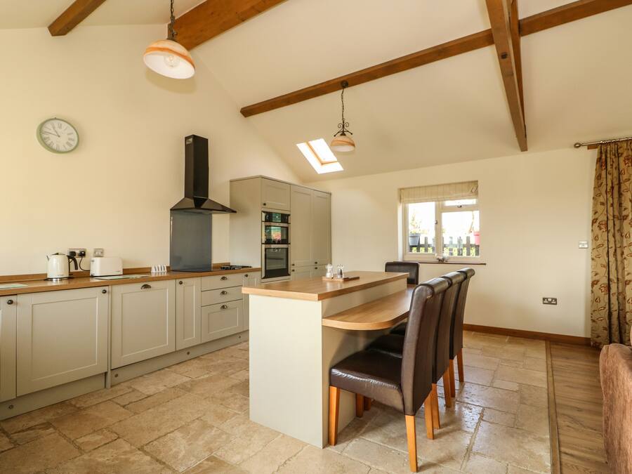 A kitchen with a central island, wooden ceiling beams, a stove, and a window with a view.