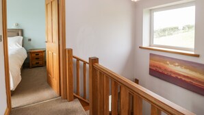 A staircase with wooden railings leading to a bedroom with a bed and a nightstand.