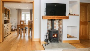 A living room with a fireplace, wooden furniture, a television, and a kitchen area.