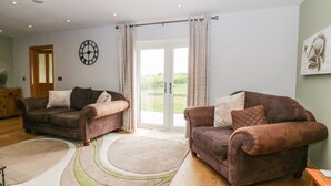 A spacious living room with two brown sofas, a large rug, and a door leading to a balcony.