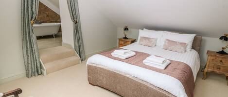 A bedroom with a large bed, a wooden nightstand, a chair, and a bathroom with a bathtub.