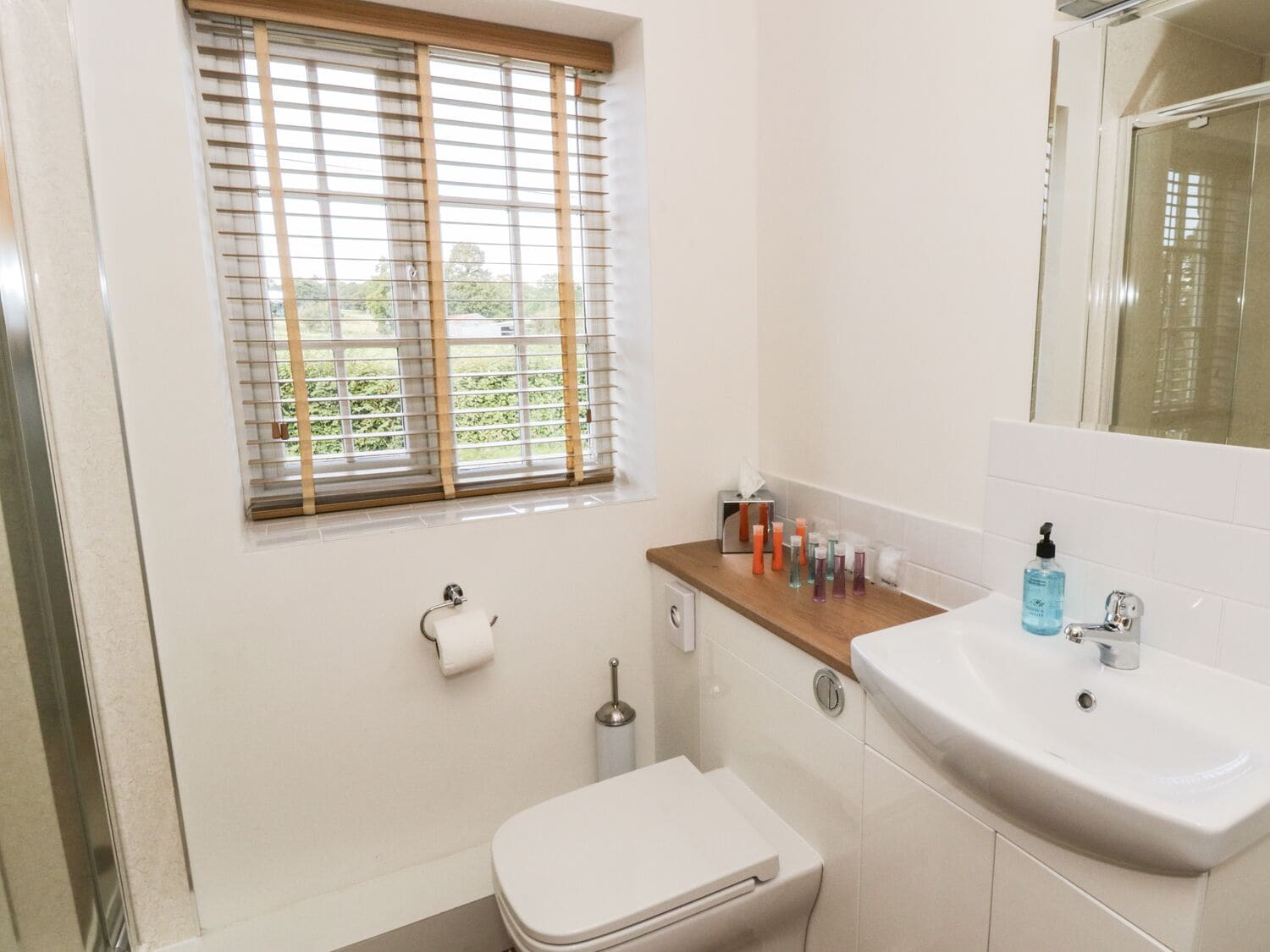 Une salle de bain équipée de toilettes, d’un lavabo et d’une fenêtre avec stores.