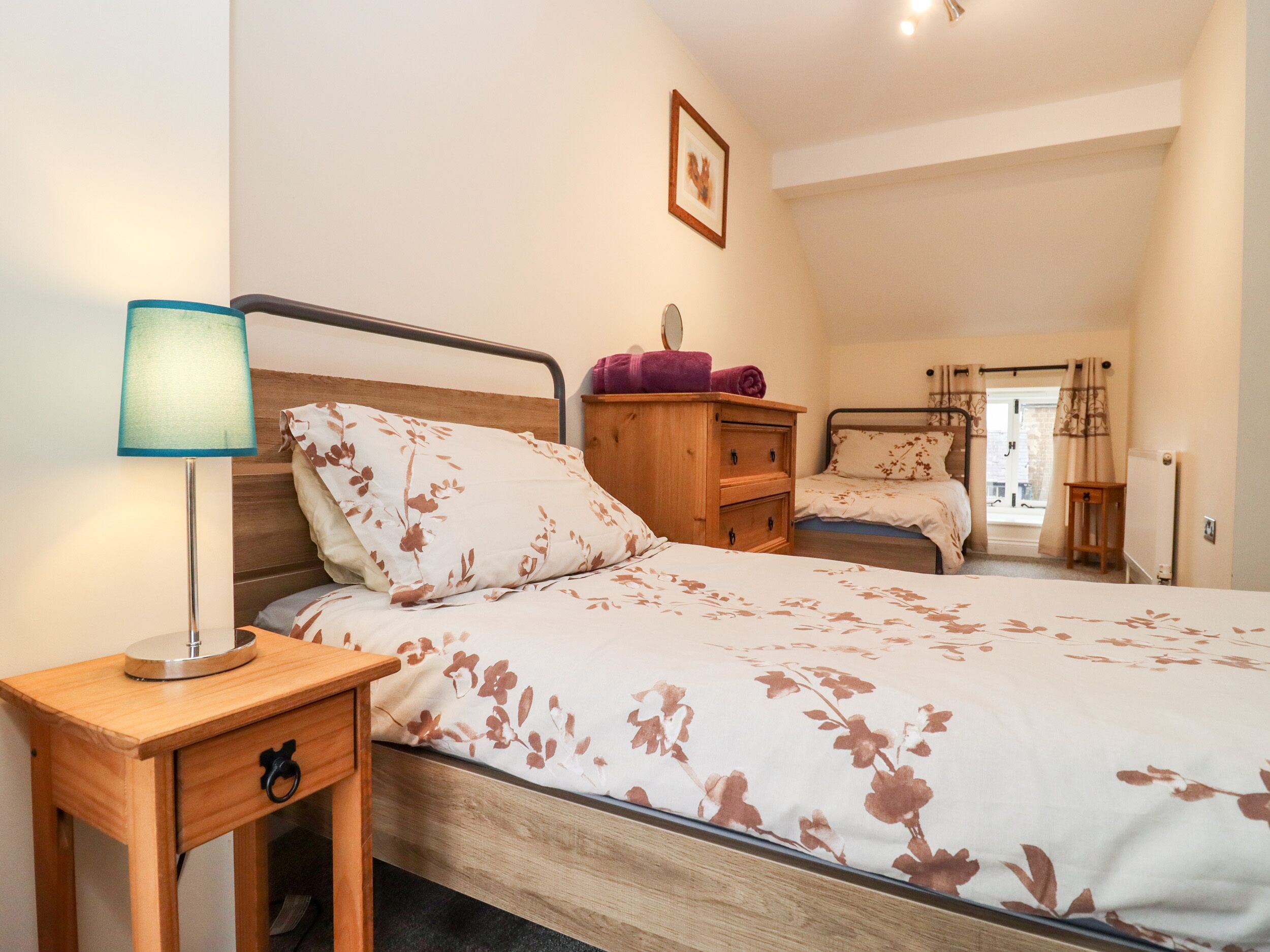 A bedroom with two beds, a wooden nightstand, a lamp, and a dresser.