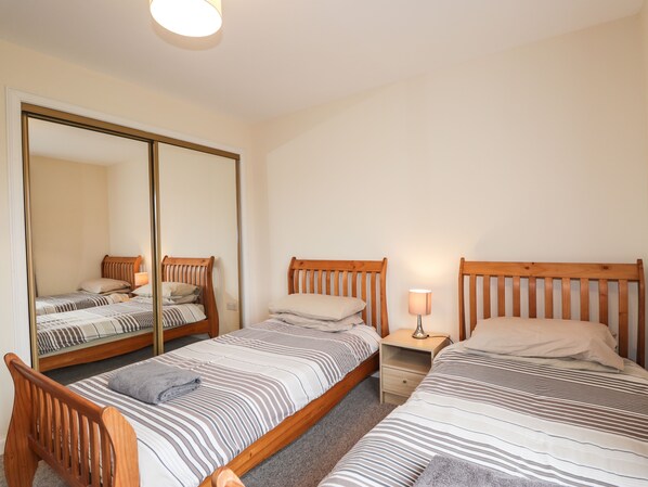 A bedroom with two single beds, a nightstand with a lamp, and a large mirror. - Hilltop (Clachtoll)