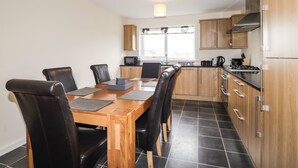 A modern kitchen with a dining area, featuring a wooden table, black chairs, and a built-in oven. - Hilltop (Clachtoll)