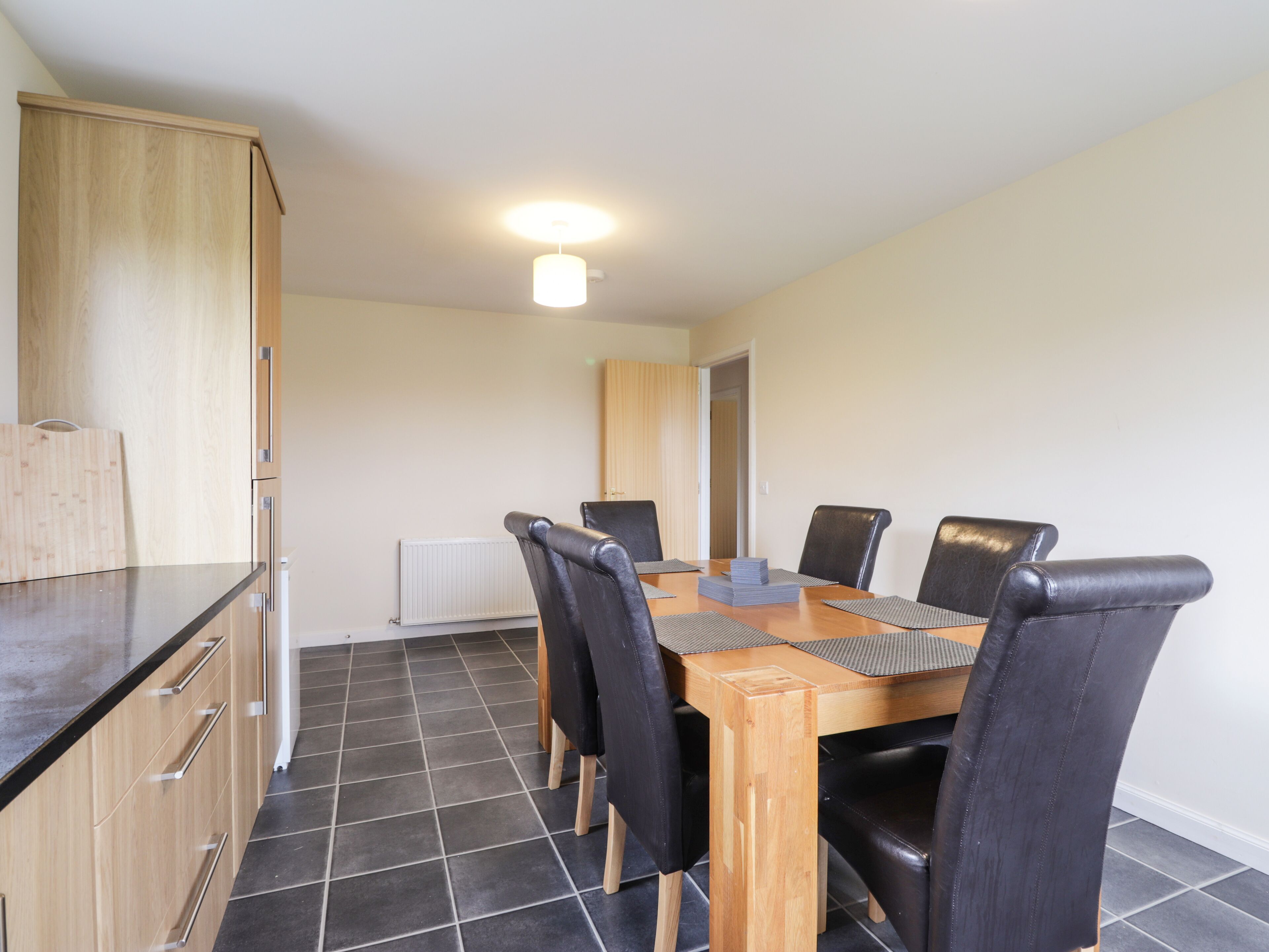 Un espace repas avec une table en bois, des chaises noires et un luminaire suspendu au plafond.