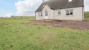 A single-story house with a sloped roof, a front door, and a small porch. - Hilltop (Clachtoll)