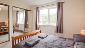 A bedroom with a bed, a window with curtains, a mirror, and a radiator. - Hilltop (Clachtoll)