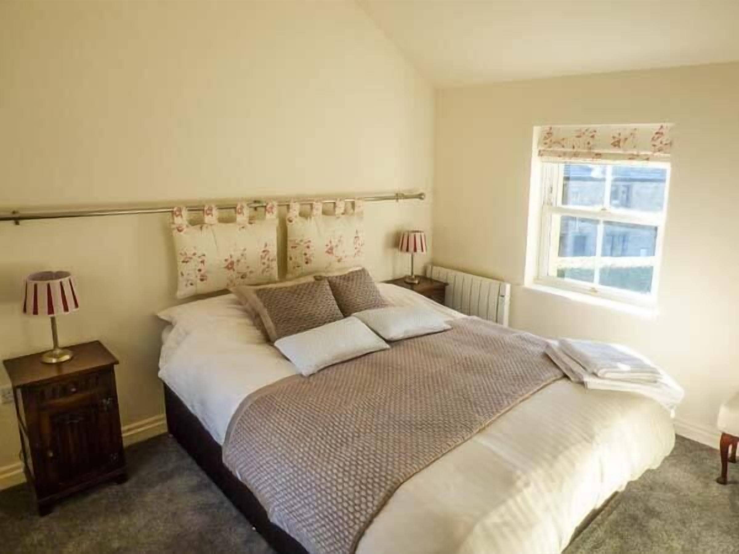 A bedroom with a bed, two bedside tables, a radiator, and a window with curtains.