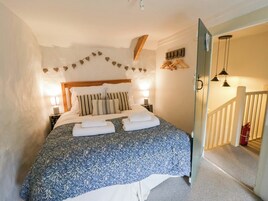 Un dormitorio con cama, lámparas de noche, cabecera de madera, perchero en la pared y una escalera que lleva a otra habitación.