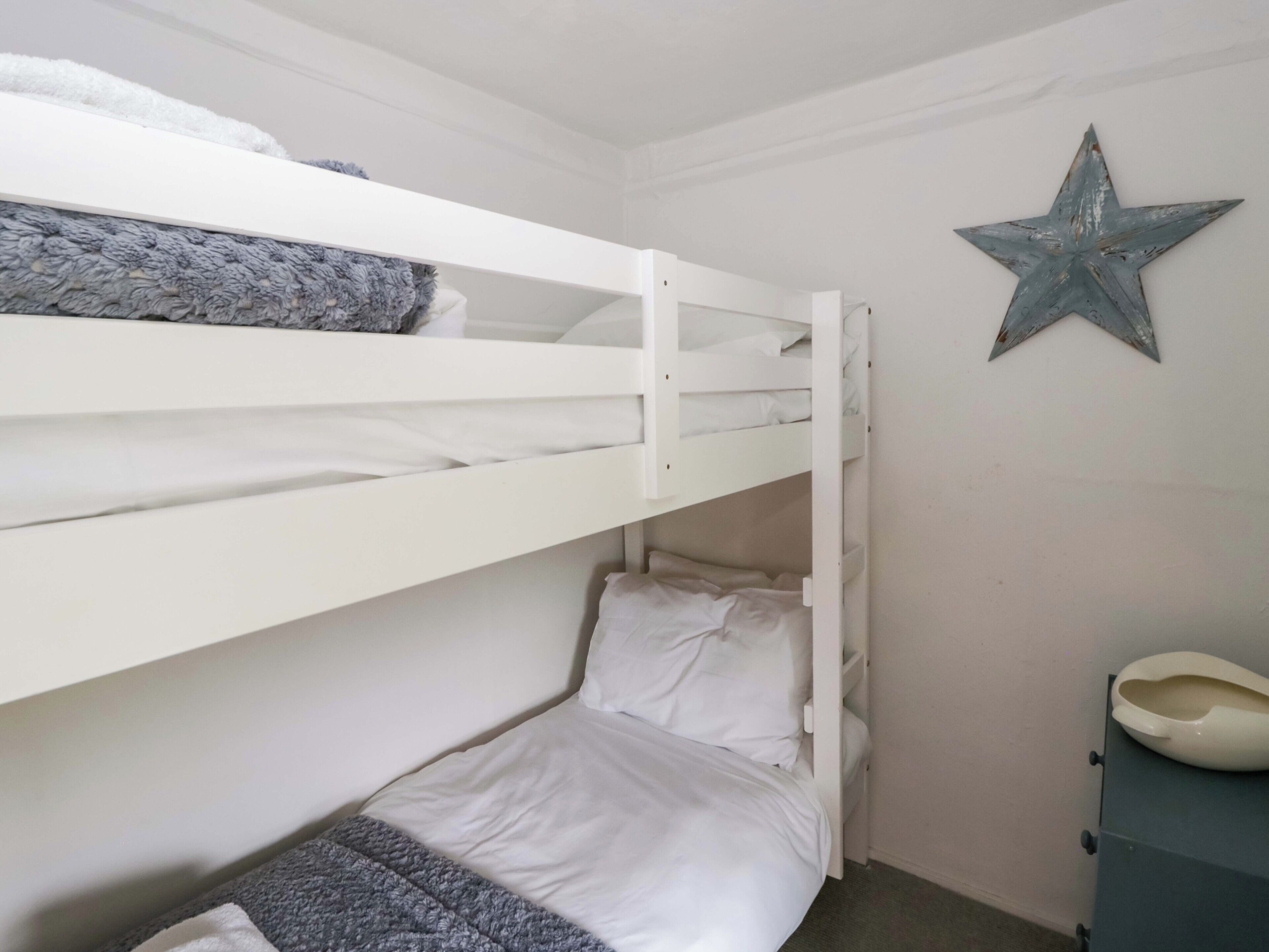 A bunk bed with white bedding, a gray blanket, and a star decoration on the wall.