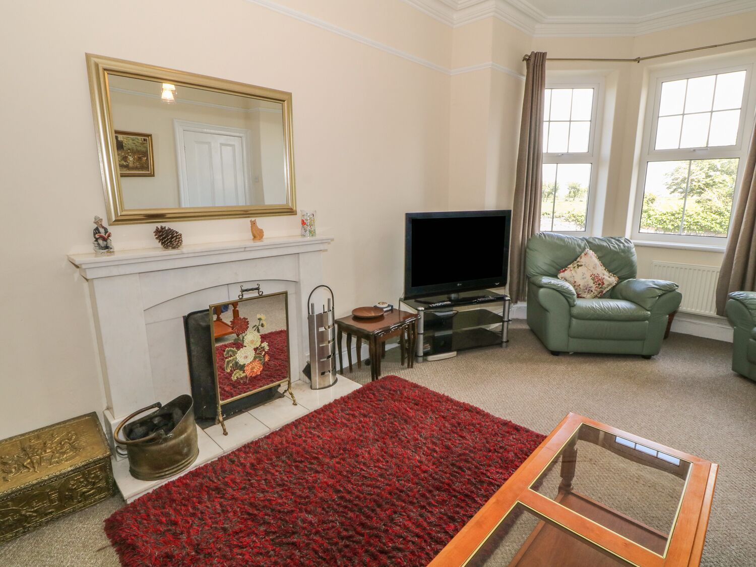 A living room with a fireplace, television, green armchair, and a red carpet.