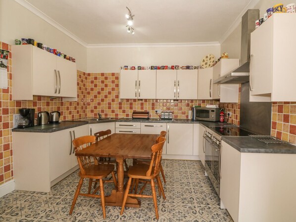 Una cocina compacta con armarios blancos, salpicadero de azulejos, una mesa de comedor con sillas y un microondas.