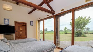 A bedroom with two beds, a television, and a door leading to an outdoor area. - The Barn (Ellesmere)