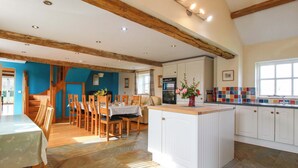 A spacious kitchen with a central island, wooden beams, and a dining area with chairs and a table. - The Barn (Ellesmere)