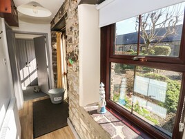 Una habitación con pared de piedra, puerta de madera, ventana con vistas al exterior y un balde en el suelo.