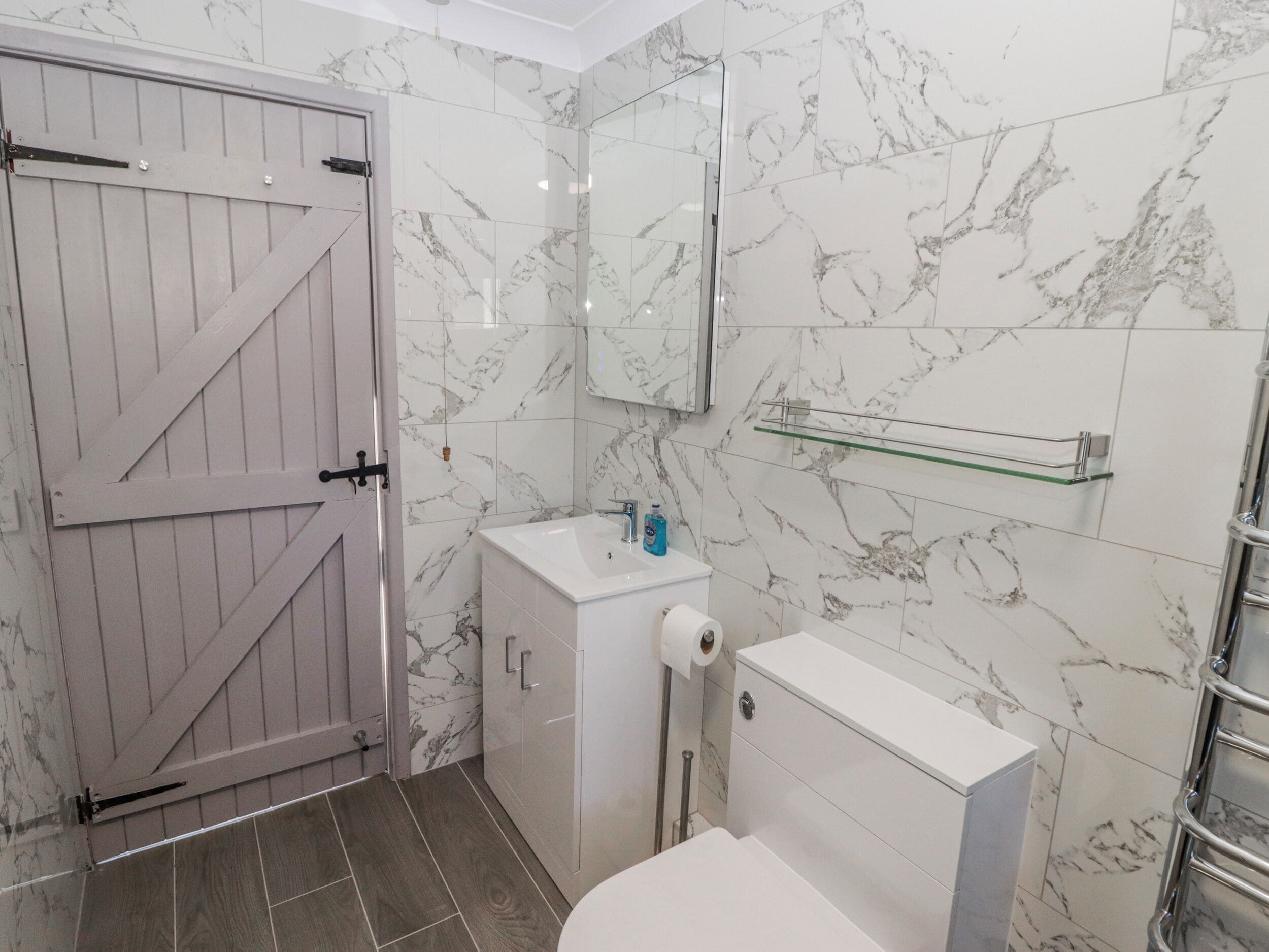 Un baño con puerta de madera, un lavamanos blanco, un espejo y un inodoro.
