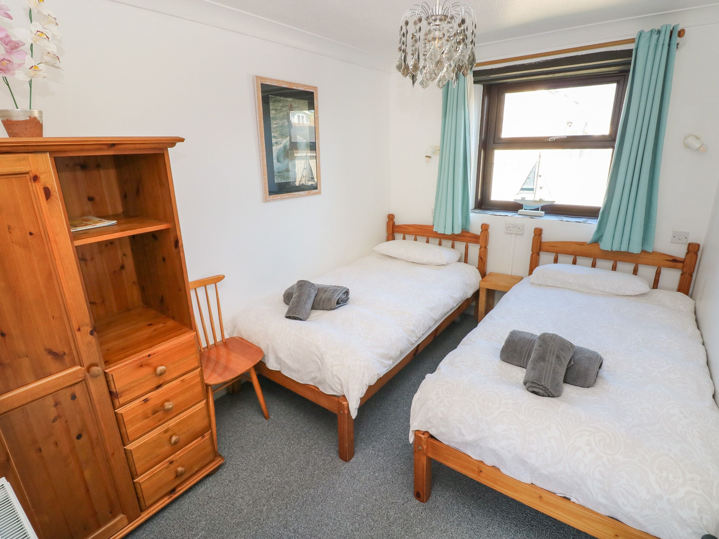 A bedroom with two wooden beds, a wooden dresser, a chair, a window with curtains, and a chandelier.