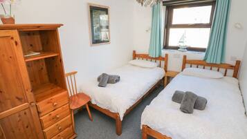 A bedroom with two wooden beds, a wooden dresser, a chair, a window with curtains, and a chandelier.