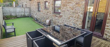 A stone house with a wooden deck, outdoor seating, and a barbecue area.