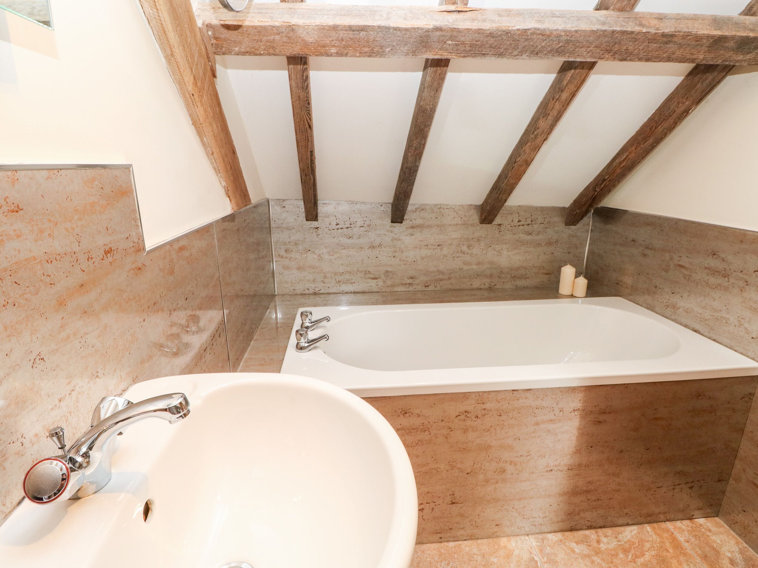 A bathroom with a bathtub, a sink, and wooden beams above.
