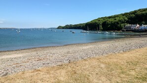 A beach with boats, a rocky shore, and a forested hill with buildings. - The Long Barn (Haverfordwest)