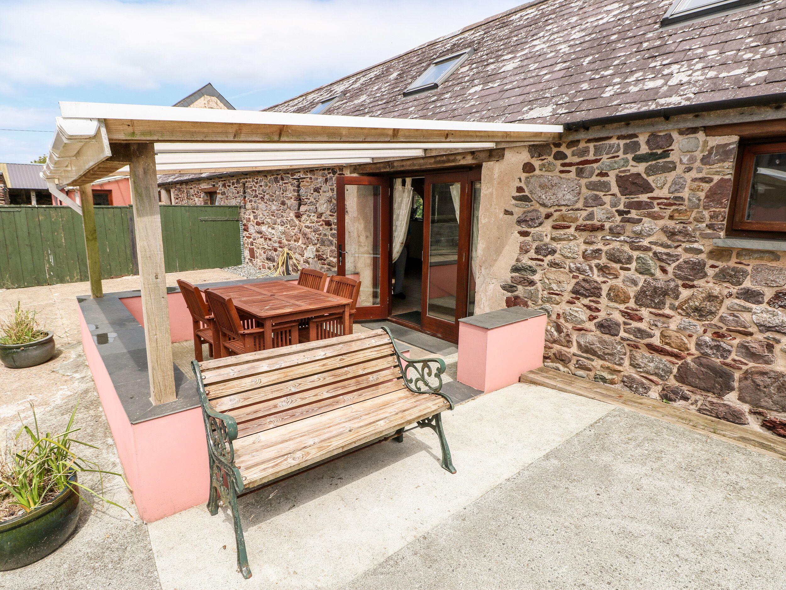 A stone building with a covered patio, wooden furniture, and a bench.