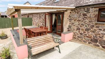 A stone building with a covered patio, wooden furniture, and a bench.