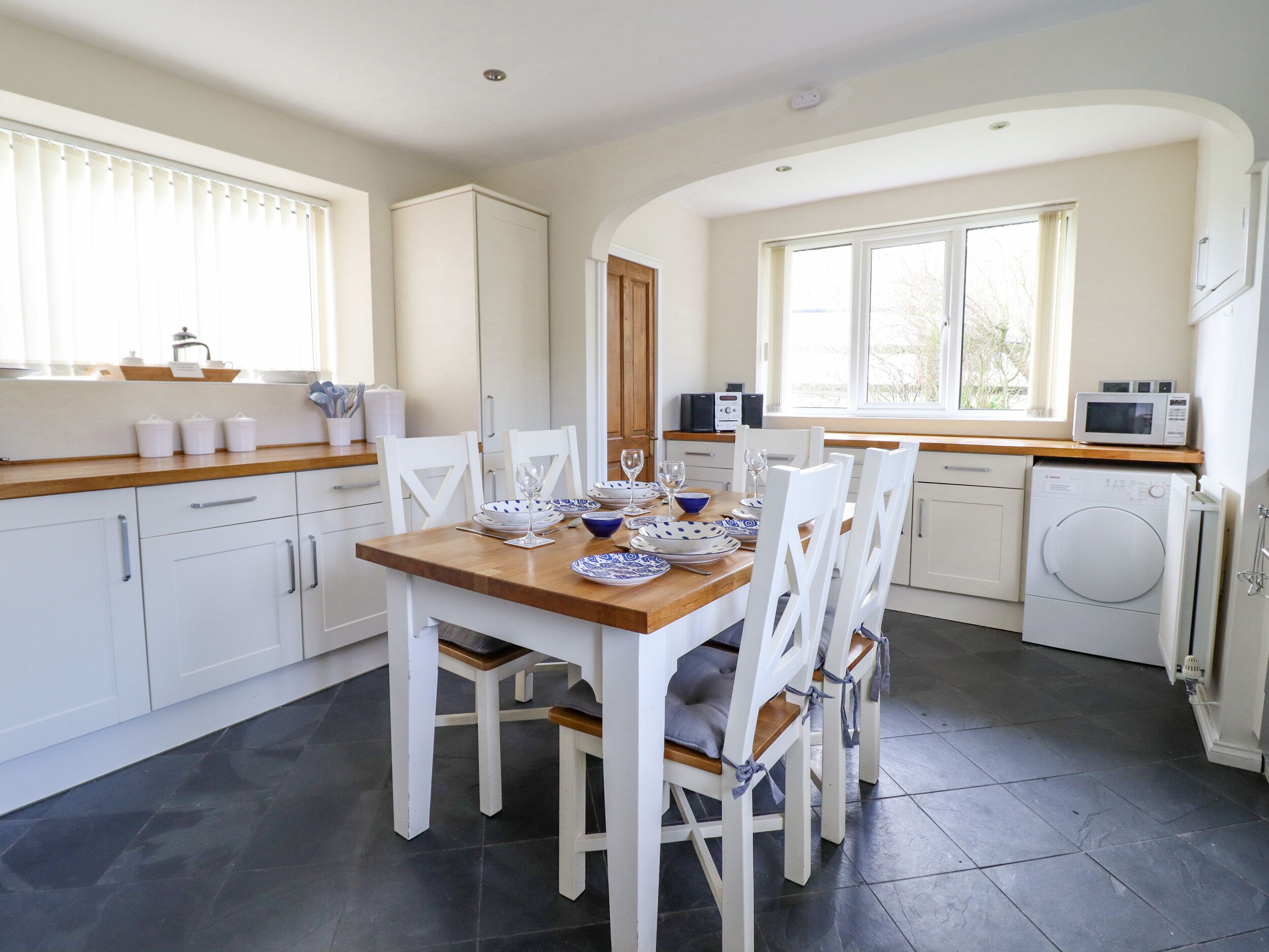 A modern kitchen with white cabinetry, a wooden dining table set for four, and a built-in washing machine.
