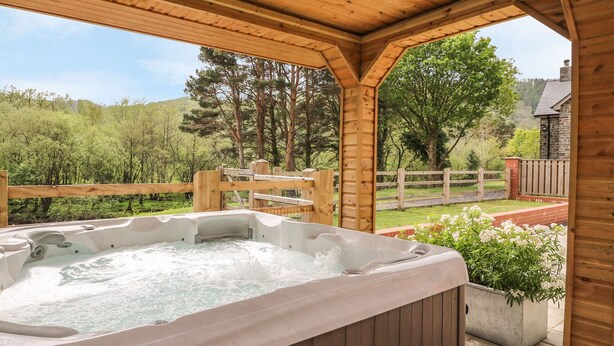 Een houten jacuzzi in een overdekte buitenruimte met uitzicht op een bebost landschap.