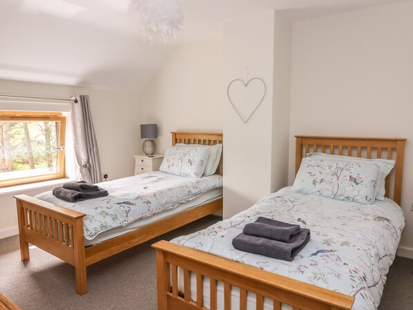 A bedroom with two wooden beds, each with floral bedding and pillows, a bedside table with a lamp, and a heart-shaped decoration on the wall. - The Farmhouse (Aberystwyth)