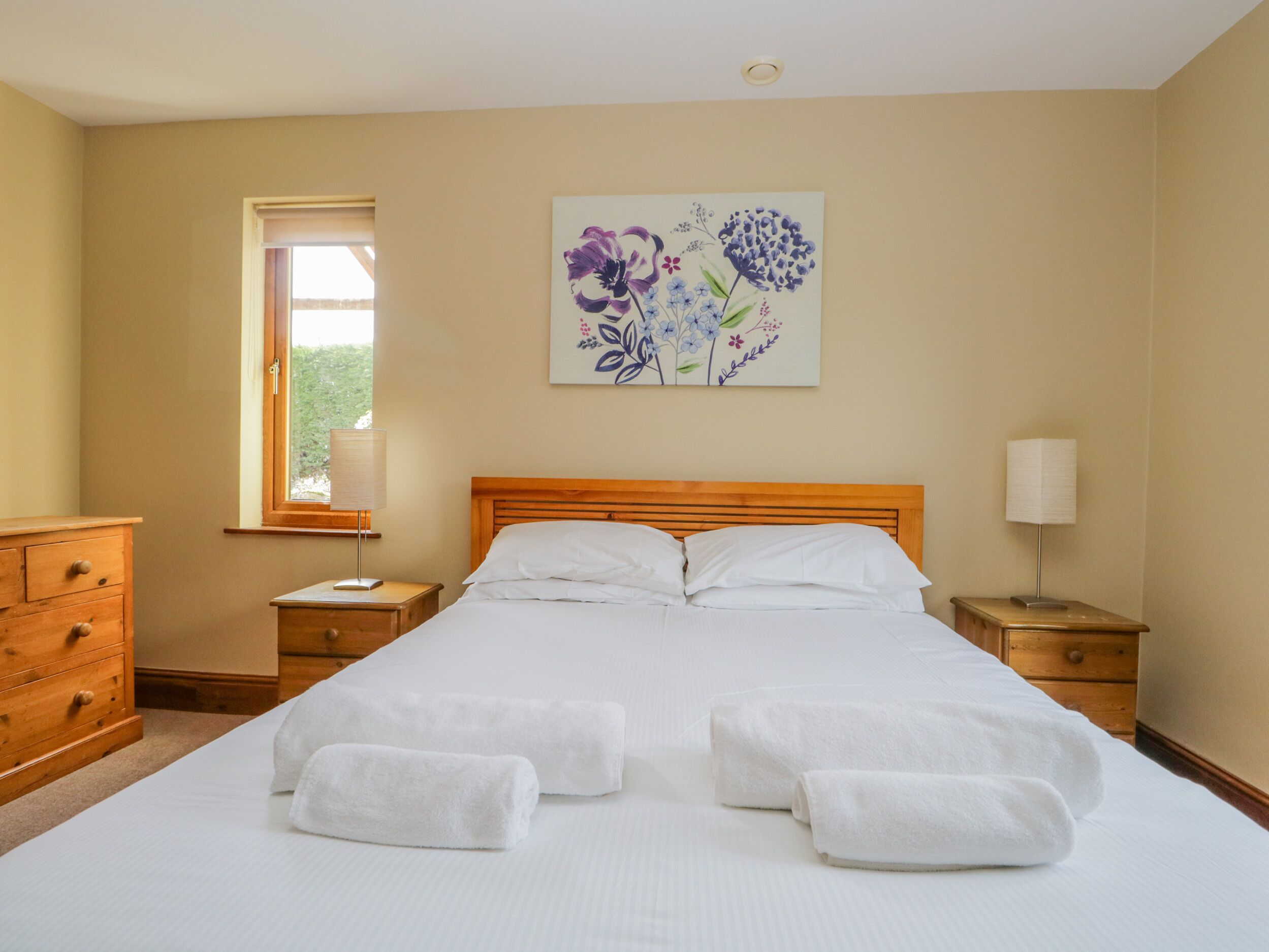 Ein ordentlich bezogenes Bett mit weißen Leinen und Handtüchern, ein hölzerner Kopfseitenverkleidung und ein Blumenbild an der Wand.