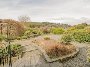 Escape to a serene outdoor oasis with a gravel pathway leading to a deck surrounded by lush greenery and rolling hills.
