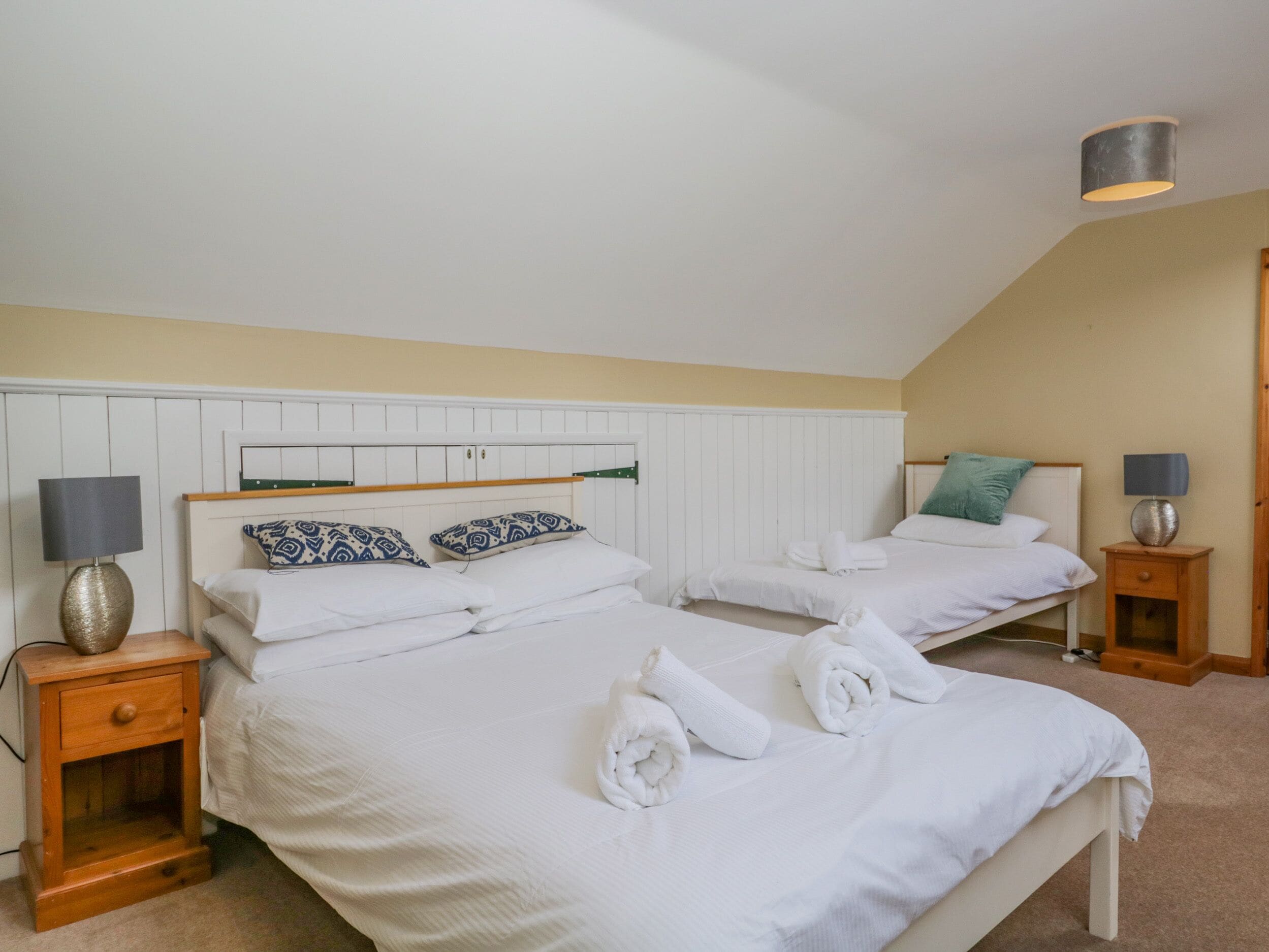 A twin bedroom with two beds, white bedding, patterned pillows, bedside lamps, and a wooden nightstand.