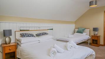 A twin bedroom with two beds, white bedding, patterned pillows, bedside lamps, and a wooden nightstand.