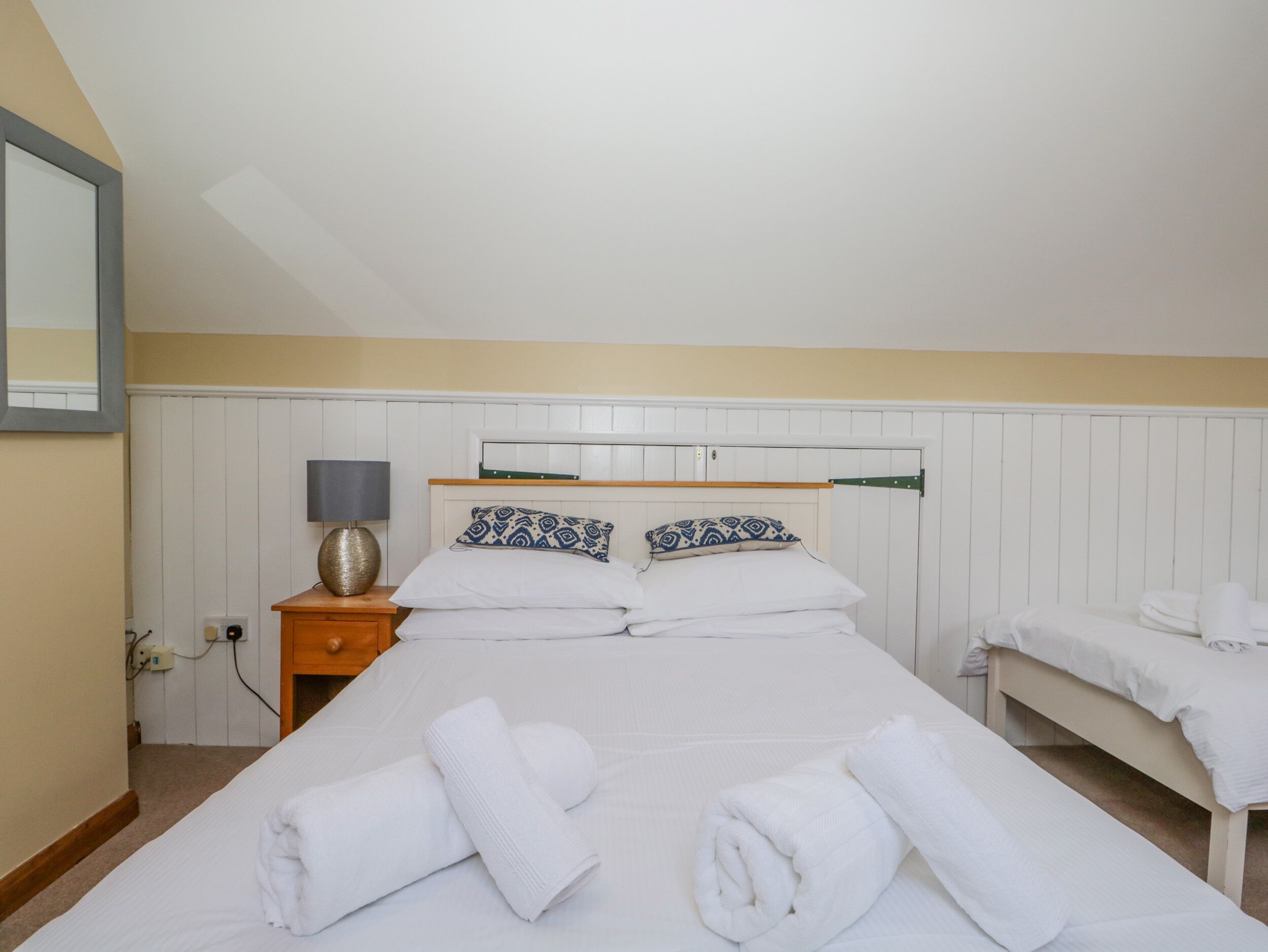 A bedroom with a bed, a bedside table, a lamp, and a mirror.