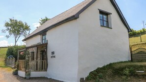 A white building with a sloped roof, a small porch with a glass door, and a sign that reads "OILS REST." - Owl's Nest (South Molton)
