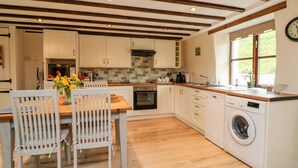 A modern kitchen with wooden beams, white cabinets, a built-in oven, and a washing machine. - Owl's Nest (South Molton)