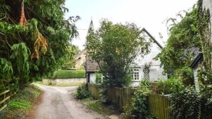 A narrow rural road flanked by lush greenery and traditional houses. - The Smithy (Leominster)