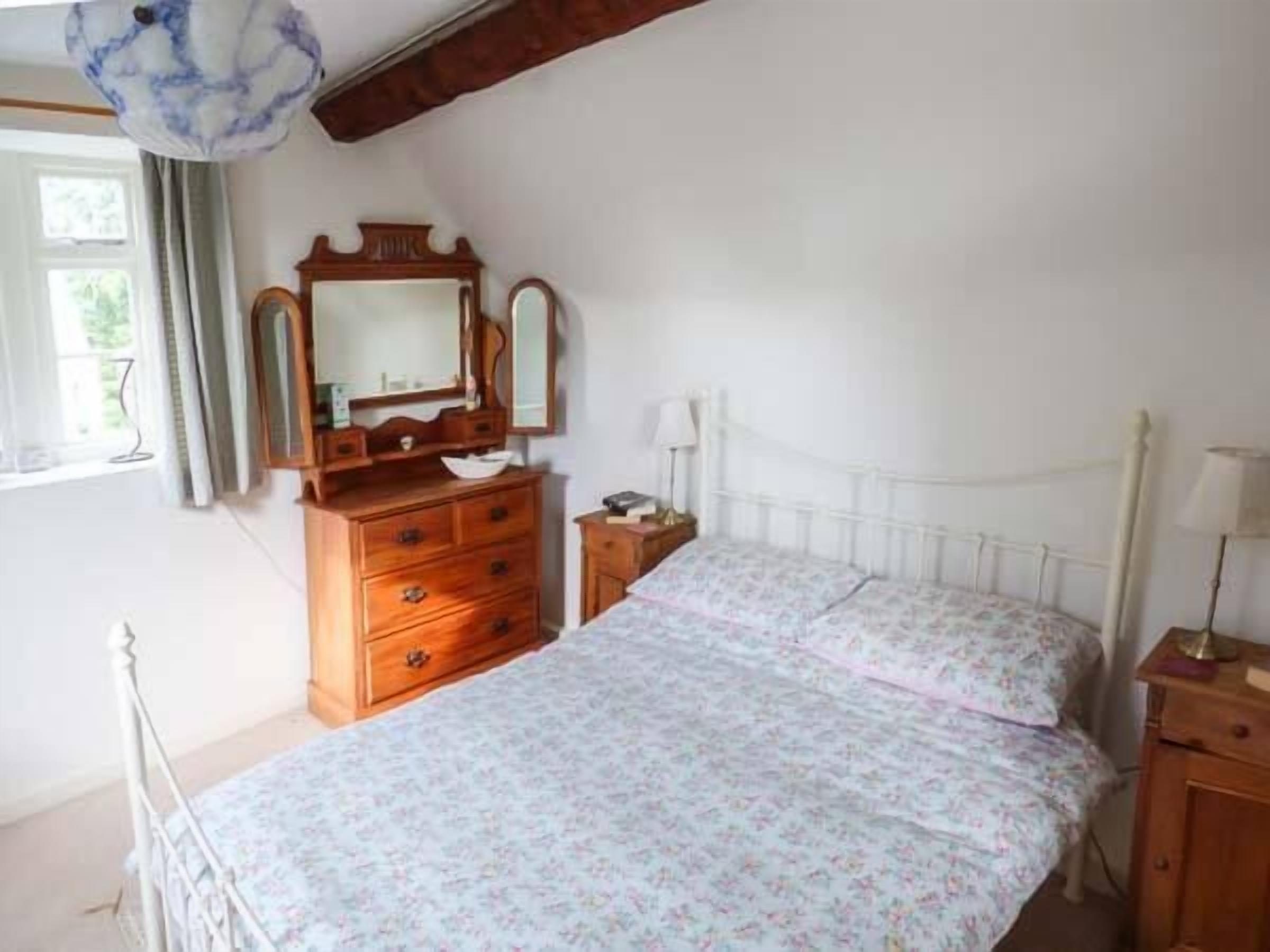 A bedroom with a bed, wooden dresser, and a mirror.