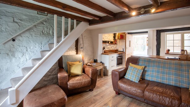 A cozy living room with a staircase, leather sofas, and a kitchen area. - Woodbine Cottage (Market Rasen)