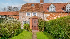 A brick house with a red-tiled roof, a wooden front door, and a small garden with a pathway leading to the entrance. - Woodbine Cottage (Market Rasen)