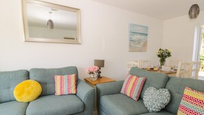 A living room with two grey sofas, one with a yellow pillow, and a dining area with a table and chairs. - White Rose Cottage (Filey)