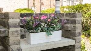 A stone planter box with flowers in front of a building with a brick facade and a lamp post. - White Rose Cottage (Filey)
