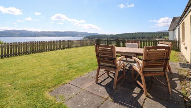 Eine Terrasse mit Tisch und Stühlen, ein Holzzaun und Blick auf einen See und Hügel.