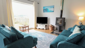A living room with two teal sofas, a TV, a fireplace, and a view of the outdoors. - Starfish Cottage (Isle of Mull)