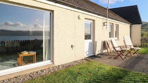 A house with a large sliding glass door, a small wooden table, and outdoor seating. - Starfish Cottage (Isle of Mull)