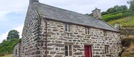 A stone house with a red door, a chimney, and a satellite dish.