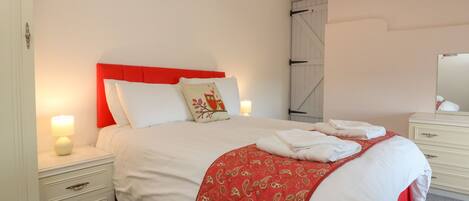 A neatly made bed with white and red bedding, a red headboard, and a single nightstand with a lamp.