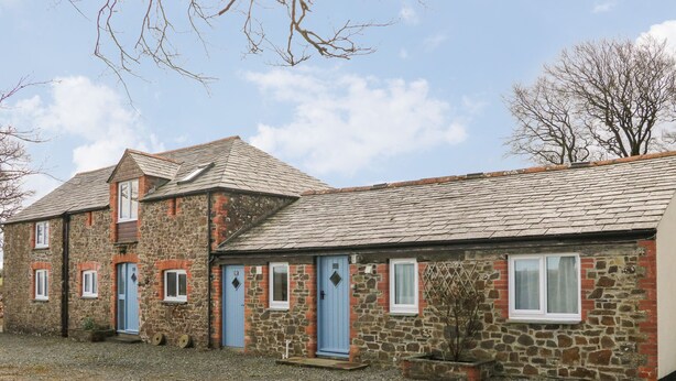 Ein Gebäude aus Stein mit mehreren Fenstern und Türen, einer Schotterauffahrt und einem Baum im Hintergrund.